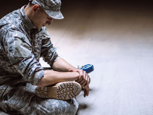 A soldier is sitting on the ground with his knees bent.